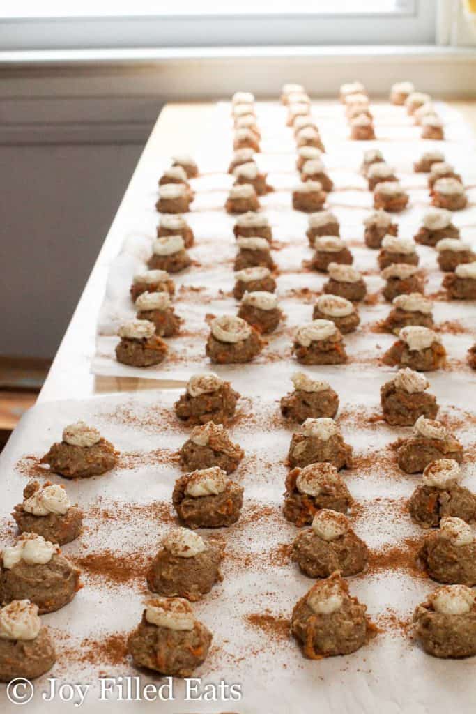 mini carrot cake cookie bites with cream cheese frosting lined on a long table with parchment paper