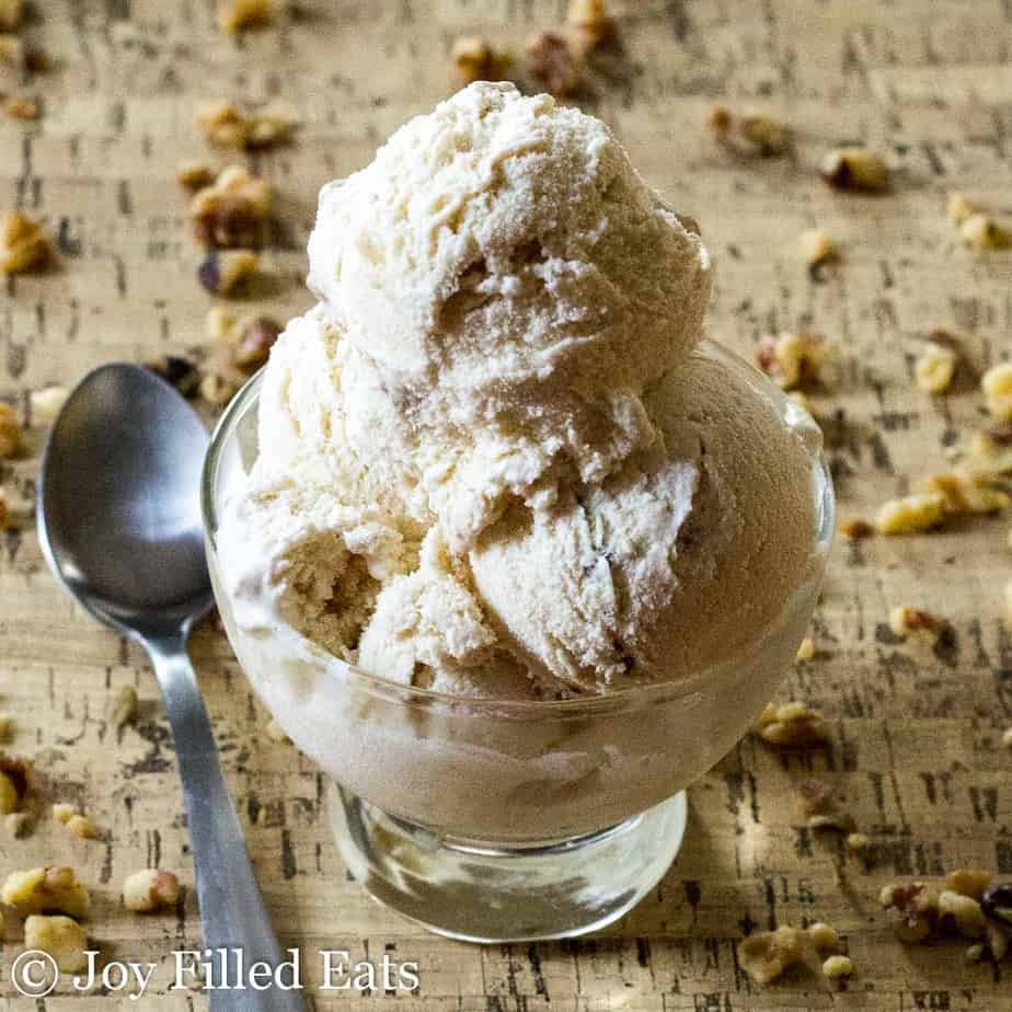 three scoops of maple ice cream with candied walnuts in an ice cream bowl placed next to a spoon