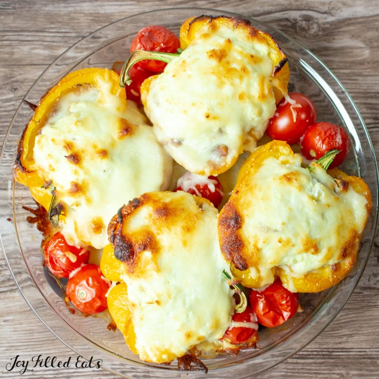 White Lasagna Stuffed Peppers and roasted cherry tomatoes in a glass pie plate on a wood surface