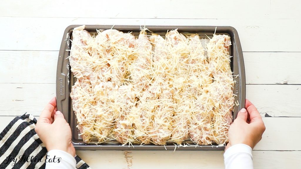 hands holding sheet pan lined with garlic parmesan chicken tenders before cooking