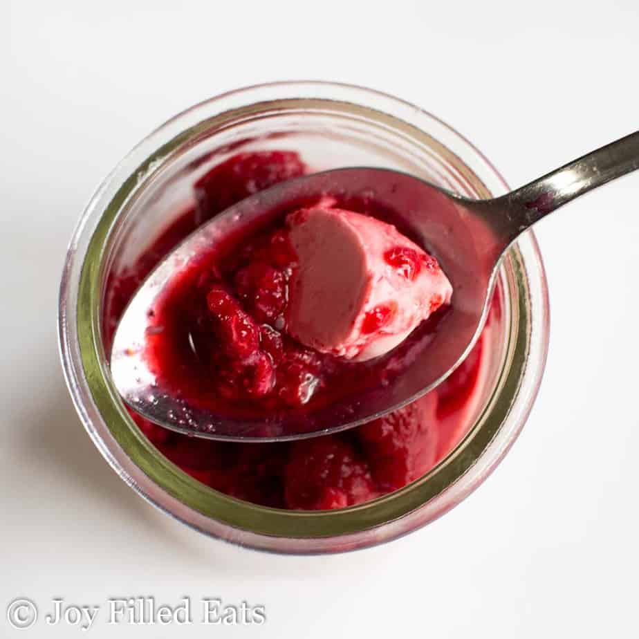 overhead view of spoon with a scoop of raspberry panna cotta hovering over a jar