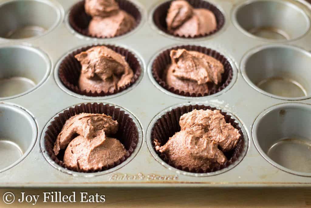 dark chocolate cupcake batter scooped into cupcake wrapper lined muffin tin