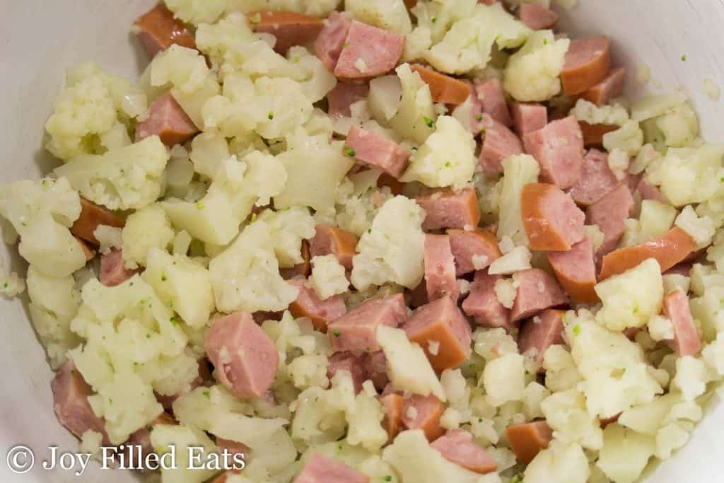 close up on large bowl of chopped cauliflower and diced smoked sausage