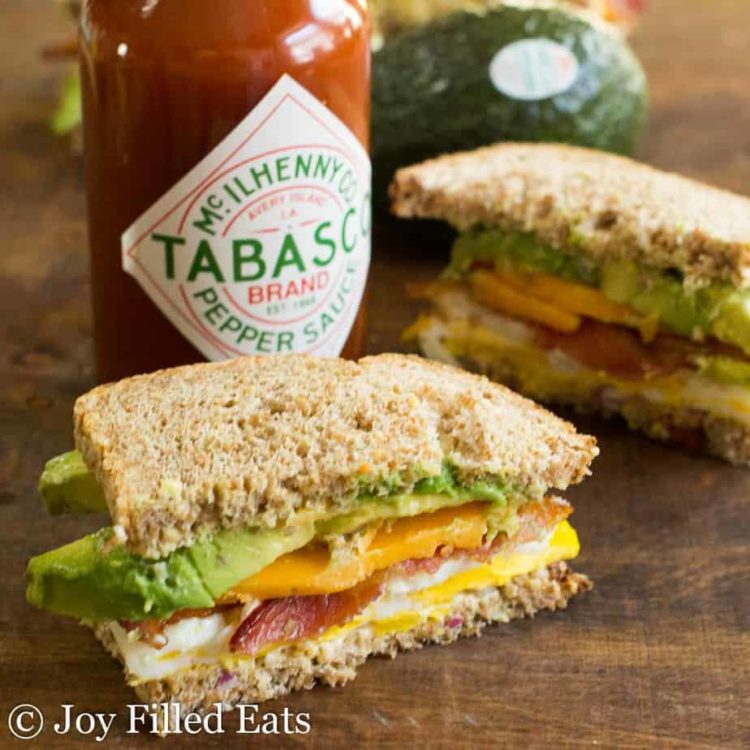 two halves of a loaded egg sandwich placed on a table with a bottle of Tabasco