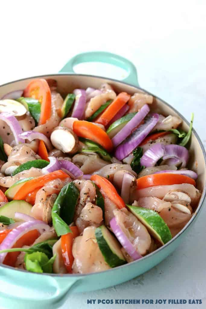 round skillet packed and layered with raw chicken and sliced vegetables