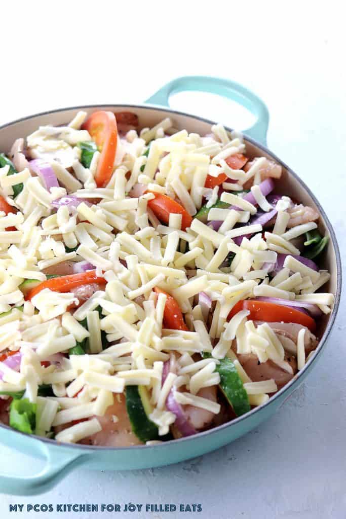 round skillet packed and layered with raw chicken and sliced vegetables topped with shredded cheese