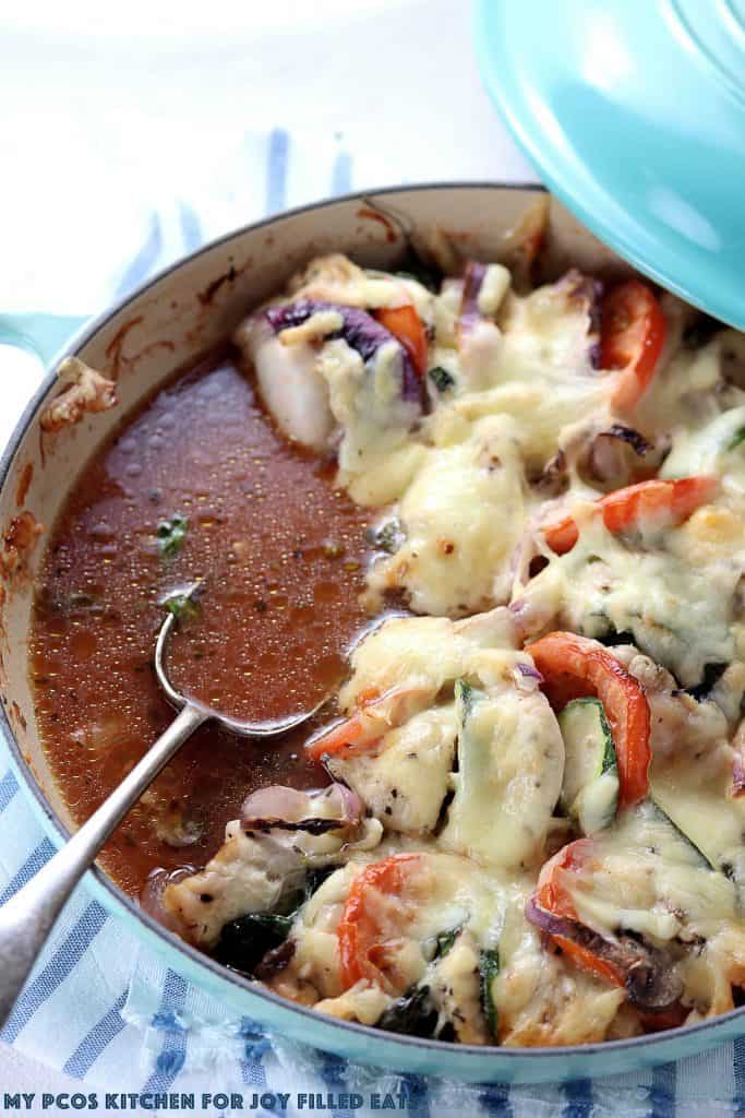 iron skillet with primavera cheesy chicken bake with serving missing and spoon placed in leftover cooking juice