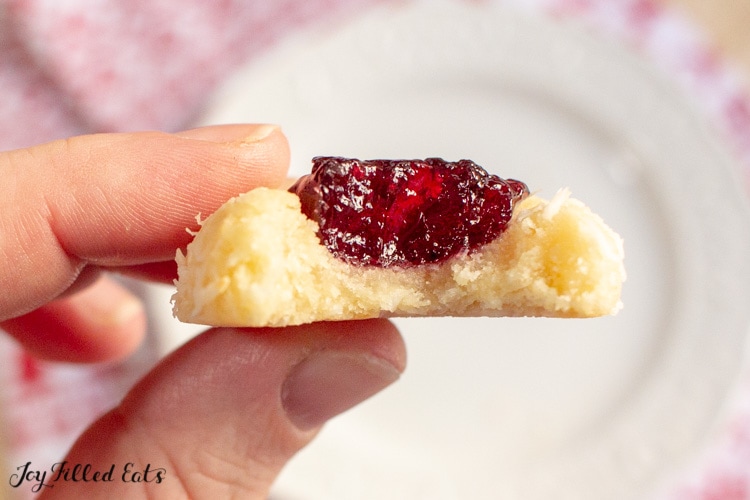 hand holding jam thumbprint cookie with bite taking out