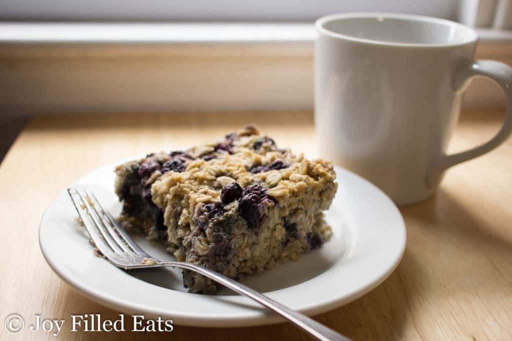 Close up of Healthy Baked Oatmeal on a white plate with a fork. cup of coffee in the background