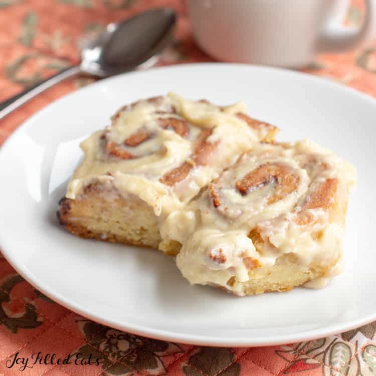 Two cinnamon rolls on a white plate on top of a floral placemat