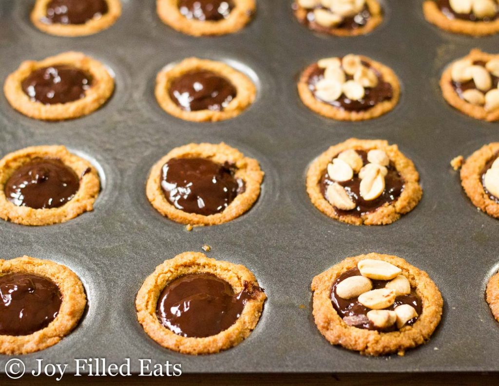 mini muffin tin filled with peanut butter cup cookies and chocolate filling, half topped with peanut pieces