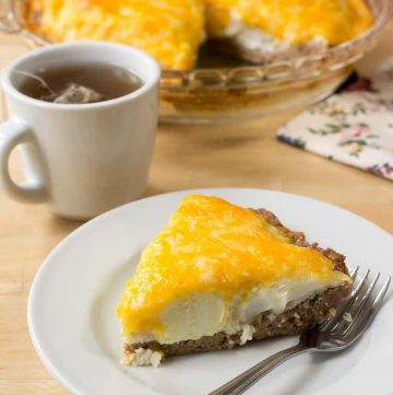 slice of sausage and egg pie on a white plate with fork next to a cup of tea