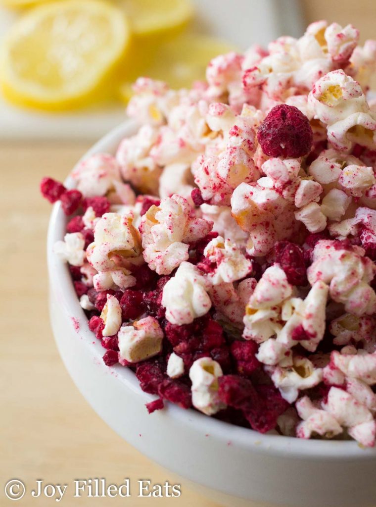 close up on bowl of raspberry lemonade popcorn topped with dried raspberry pieces set in front of lemon slices