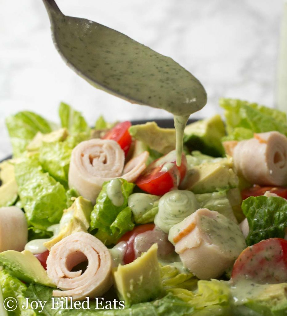 spoon drizzling paleo ranch dressing onto salad close up