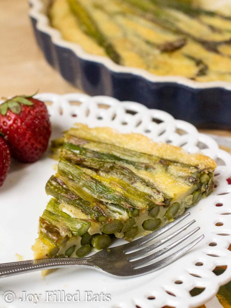 slice of asparagus quiche on a white plate with fork up close