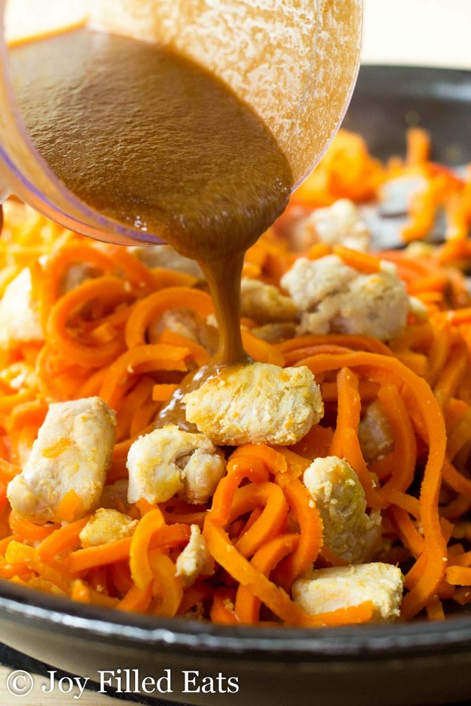 dressing being poured onto sweet ginger chicken with carrot noodles