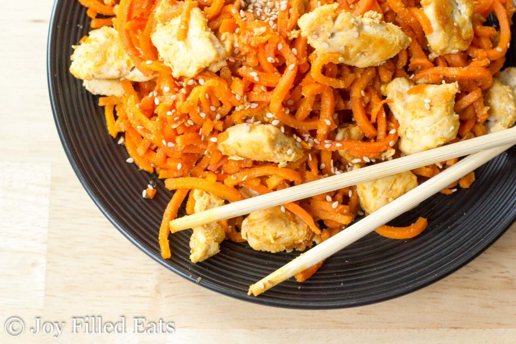 overhead view of Sweet ginger Chicken with Carrot Noodles on a black plate with chopsticks