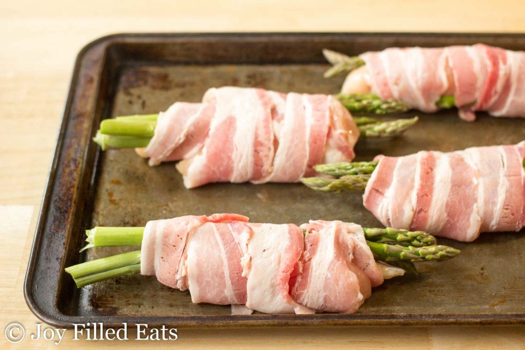 sheet pan lined with asparagus stuffed chicken wrapped in bacon before baking