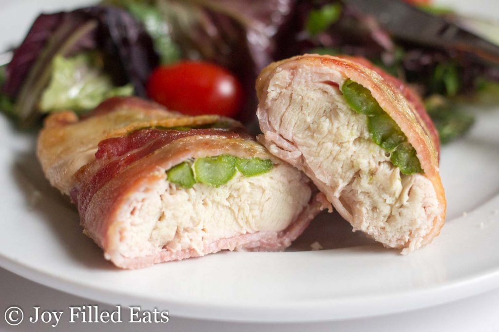 asparagus stuffed chicken wrapped in bacon cut in half to show layers on a white plate