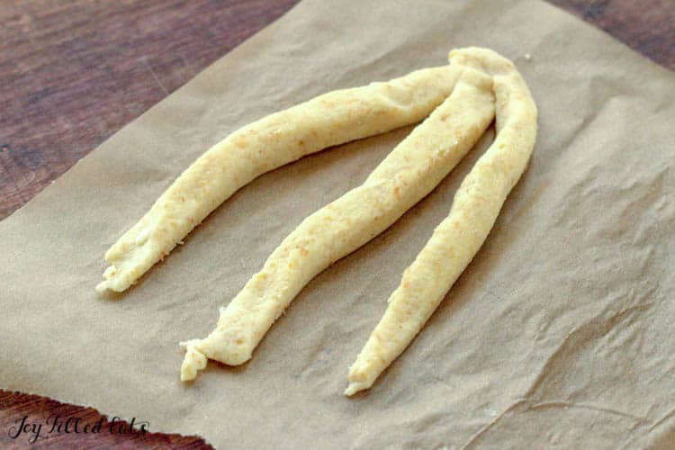 keto breadstick dough rolled into three strands before being braided on parchment paper