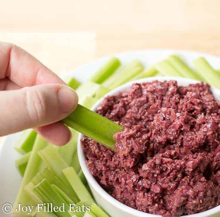 hand holding celery stick being dipped into olive tapenade