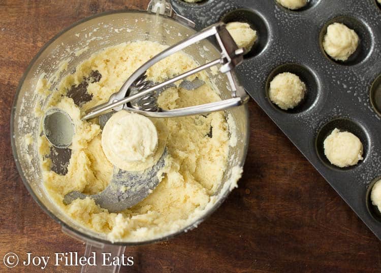 food processor full of dough and ice cream scoop next to mini muffin tin filled with balls of dough