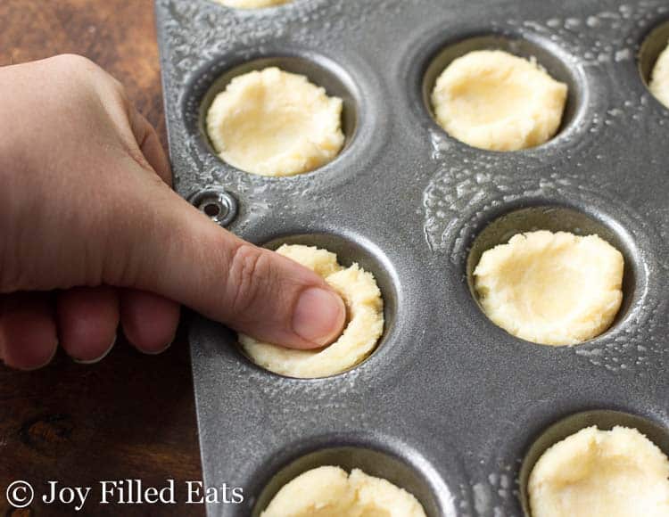 thumb pressing on dough to be shaped into cups in mini muffin tin