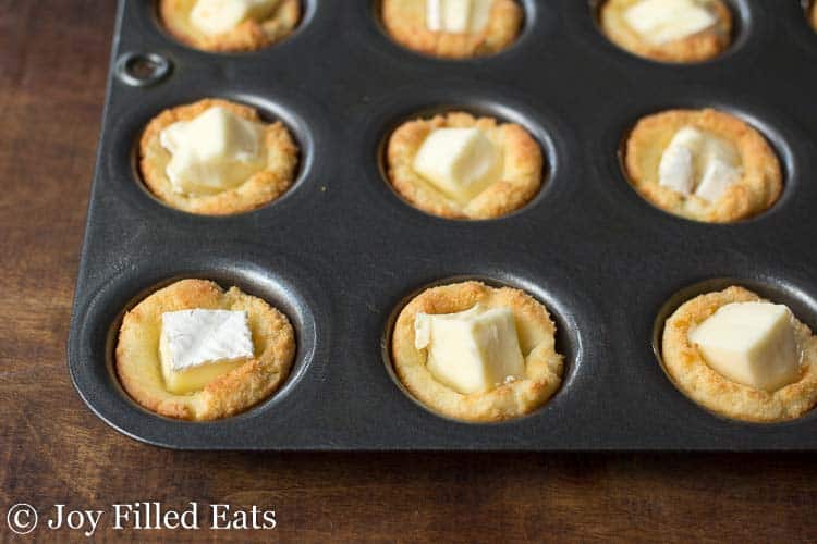 mini muffin tin filled with crust dough stuffed with cubed bites of brie