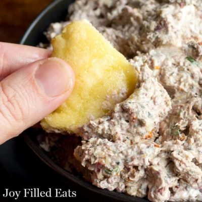 Hand dipping pita chip into bowl of Mediterranean Cheese Spread