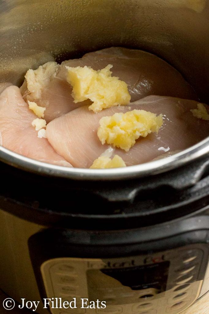raw chicken breasts in an instant pot topped with buttery coconut oil