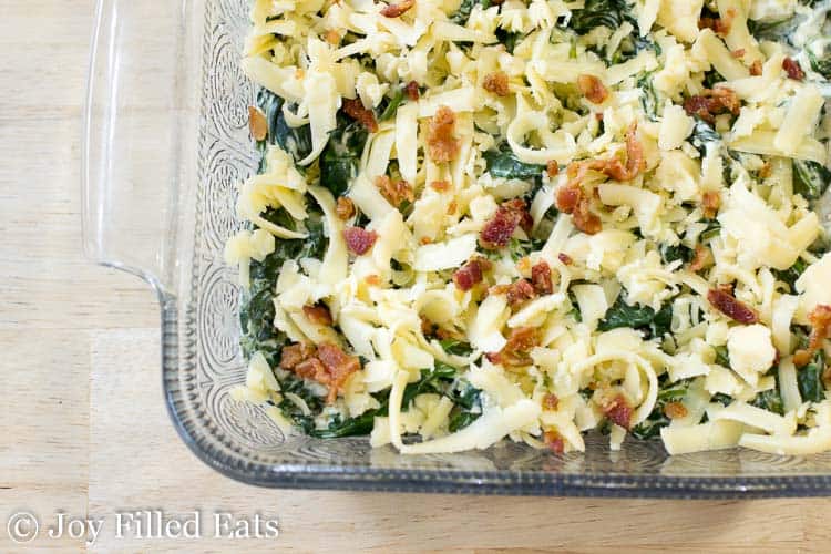 square casserole dish full of creamed spinach topped with shredded cheese and bacon pieces close up