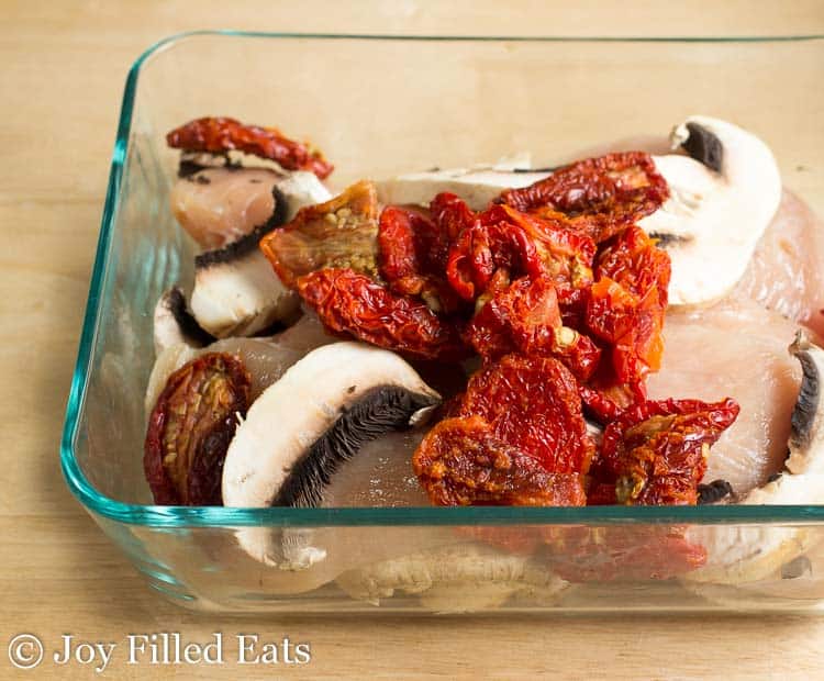 raw chicken breasts, sun-dried tomatoes and mushrooms in a glass baking dish