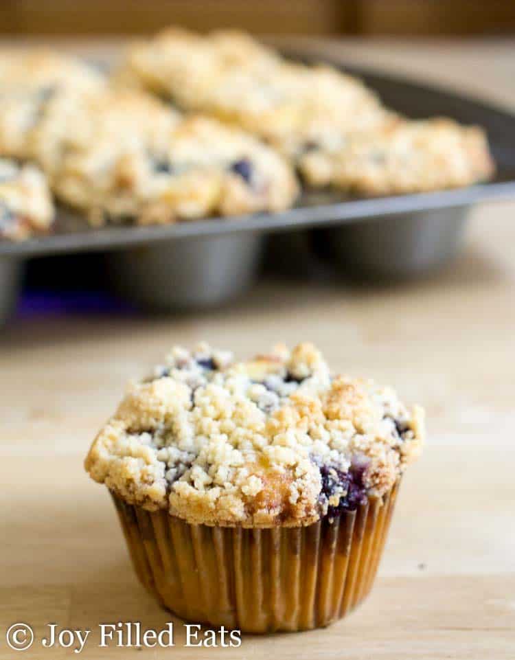 close up of blueberry muffin with crumb topping in front of muffin tin