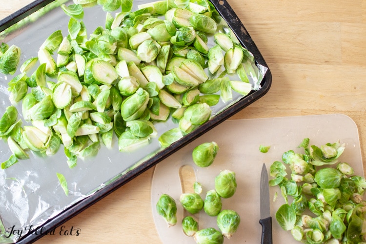 A cutting board and paring knife showing how to trim and cut the brussels sprouts