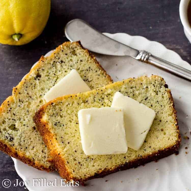 two slices of lemon poppy seed loaf cake topped with pads of butter on a white plate