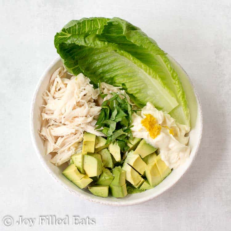 bowl full of ingredients for chicken salad with avocado wrapped in lettuce