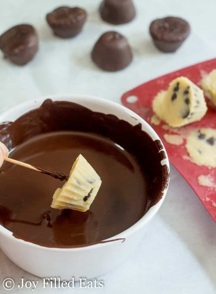 A toothpick holding a Frozen Cookie Dough Bites being dipped into a bowl of chocolate