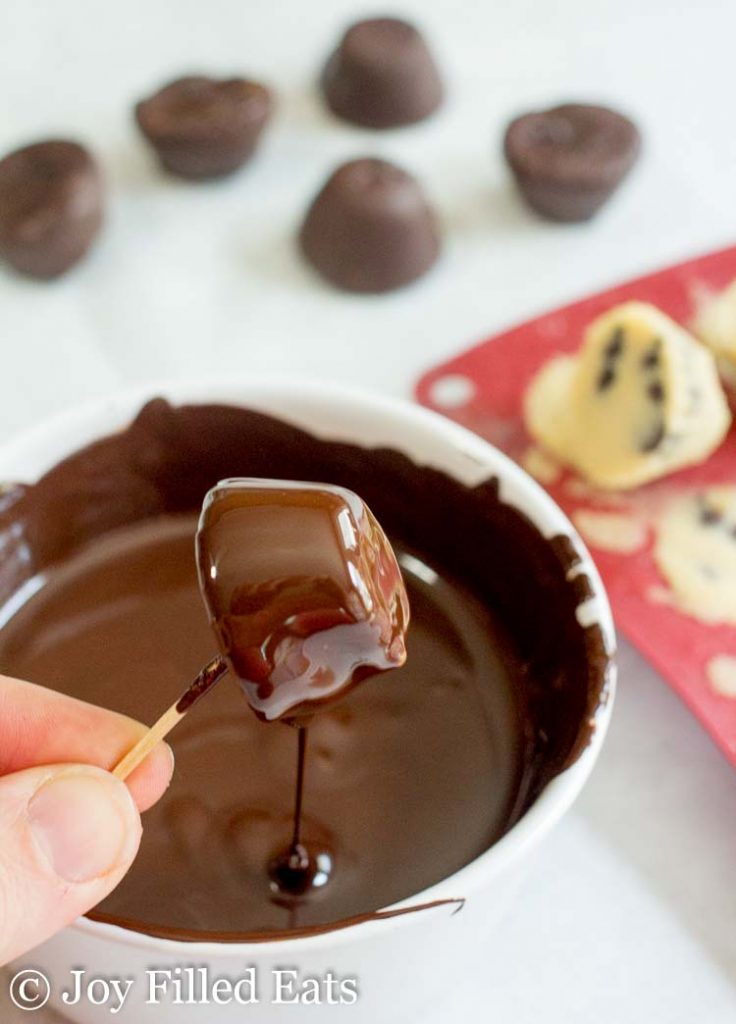 A hand holding a cookie dough bite dripping chocolate