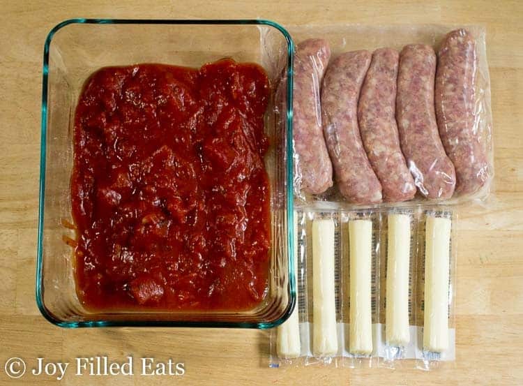overhead view of casserole dish filled with marinara sauce, a package of sausage links and a package of string cheese