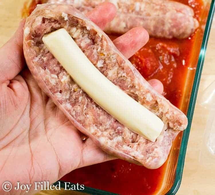 hand holding butterflied sausage link with log of cheese placed in the center