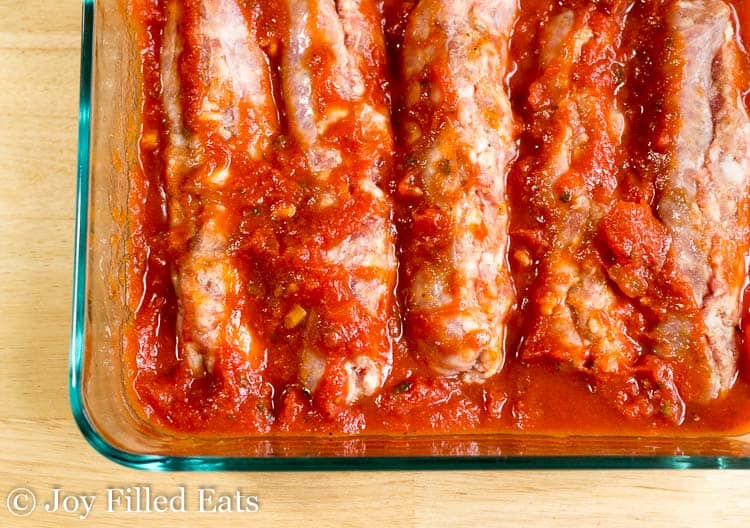 close up on casserole dish lined with sausage covered in marinara sauce