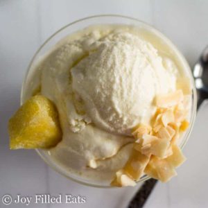 scoop of pina colada ice cream topped with coconut flakes and pineapple in a small glass bowl from above