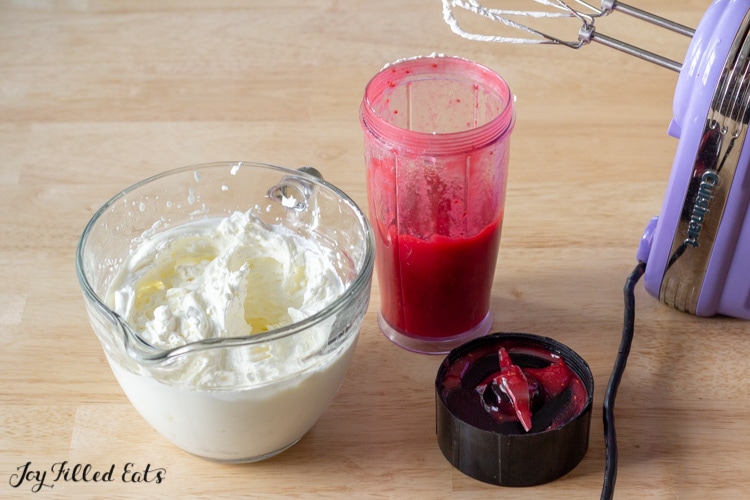 frosting in a measuring cup next to a jar of raspberry puree and hand mixer