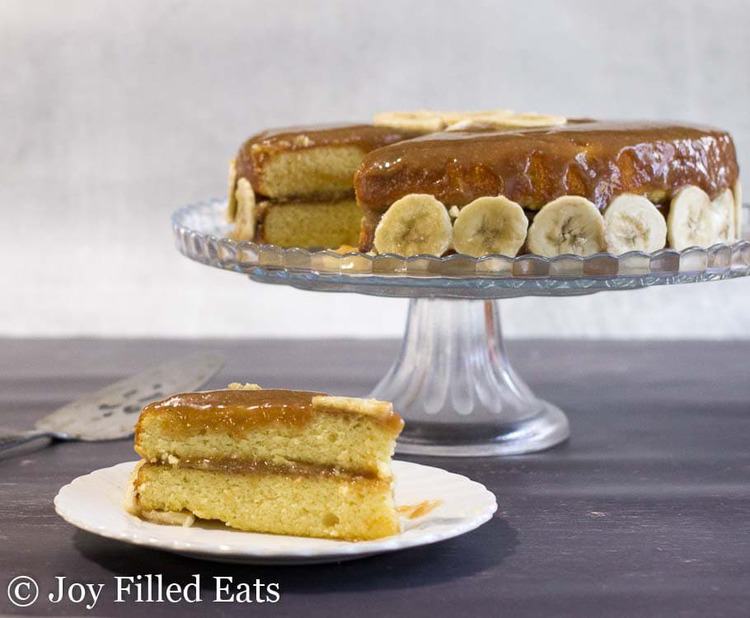 slice of banana foster cake on a white plate placed next to a cake plate with remaining banana cake