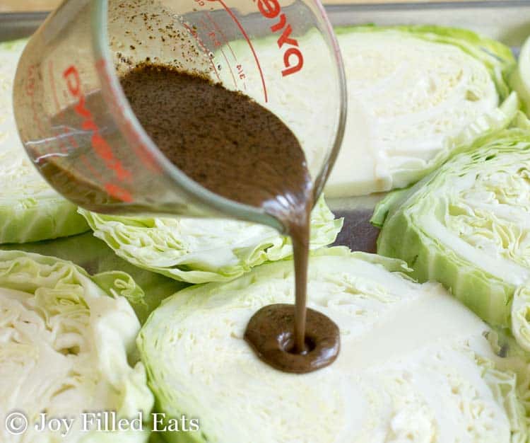 measuring cup pouring balsamic mixture onto cabbage steak
