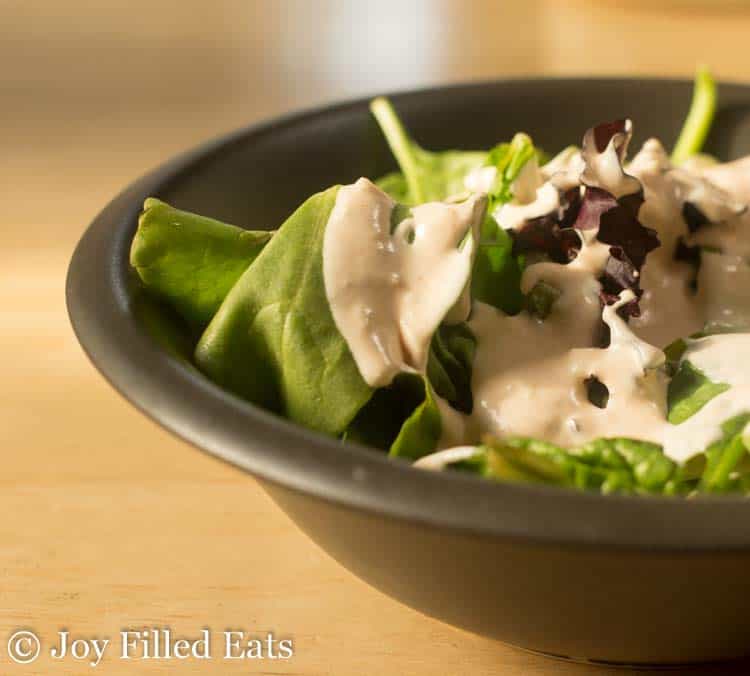 close up on bowl of mixed greens drizzled with creamy garlic salad dressing