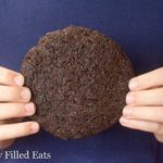 hands holding a large triple chocolate cookie against a blue shirt