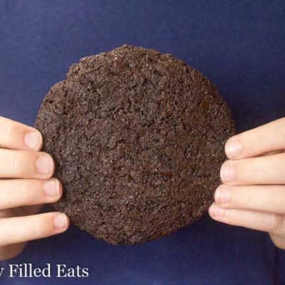 hands holding a large triple chocolate cookie against a blue shirt