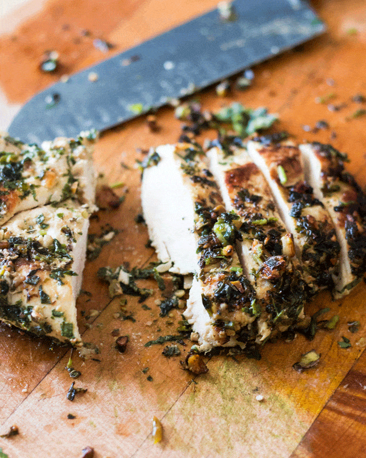 Sliced Macadamia and Sage Crusted Chicken with Sage on a wooden chopping board with a sharp knife in the background