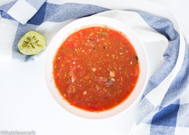 overhead view of white bowl full of salsa surrounded by a decorative napkin and half a squeezed lime